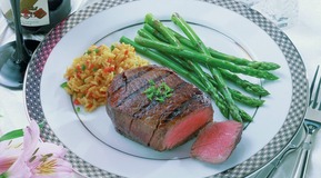 Filetsteak (medium fryed) on a plate decorated with green asparagus and rice. View on a table decoration.